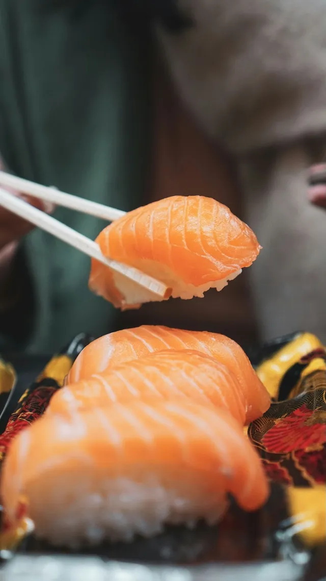 Nigiri mit Lachs, eines davon zwischen Stäbchen